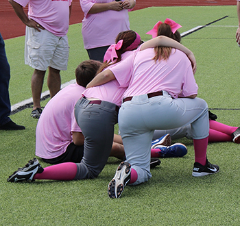 Zane Jackson, Haley Stephens and Abigail Junek with the BCS Outlaws sport their pink jerseys while sitting on the sidelines.