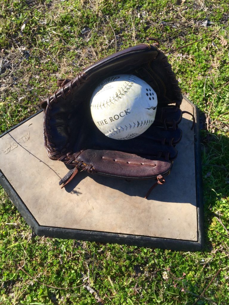 A beep baseball nestled in a baseball glove sits on home plate.