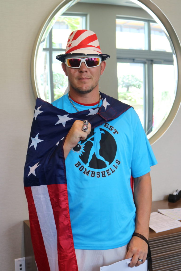 A smiling check-in table volunteer wears an American flag cape and hat.