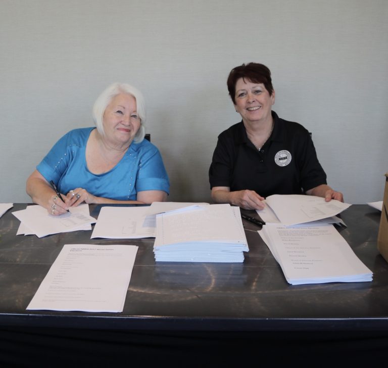 Two women volunteers smile from behind piles of voting ballots.