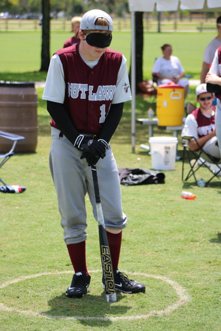 A BCS Outlaw player leans on his bat while waiting in the batting circle.