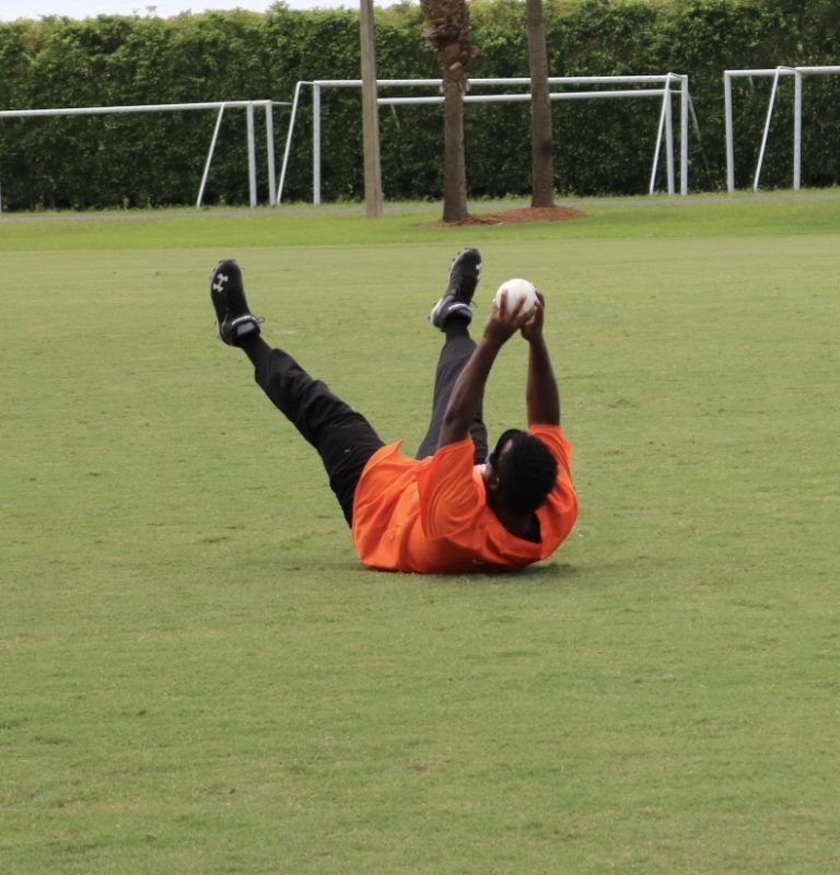 A player dressed in bright orange holds the ball high above his body while on his back.