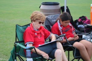 Long time Austin Blackhawks volunteer Rusty Reames is keeping score while her granddaughter Kamryn checks things out on her cellphone beside her.