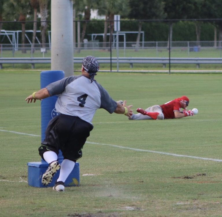 A player dressed in blue arrives at third base as a player dressed in red catches the ball.