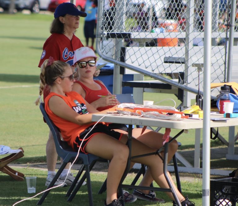 The base operator and scorekeeper focus on the game from behind a table.