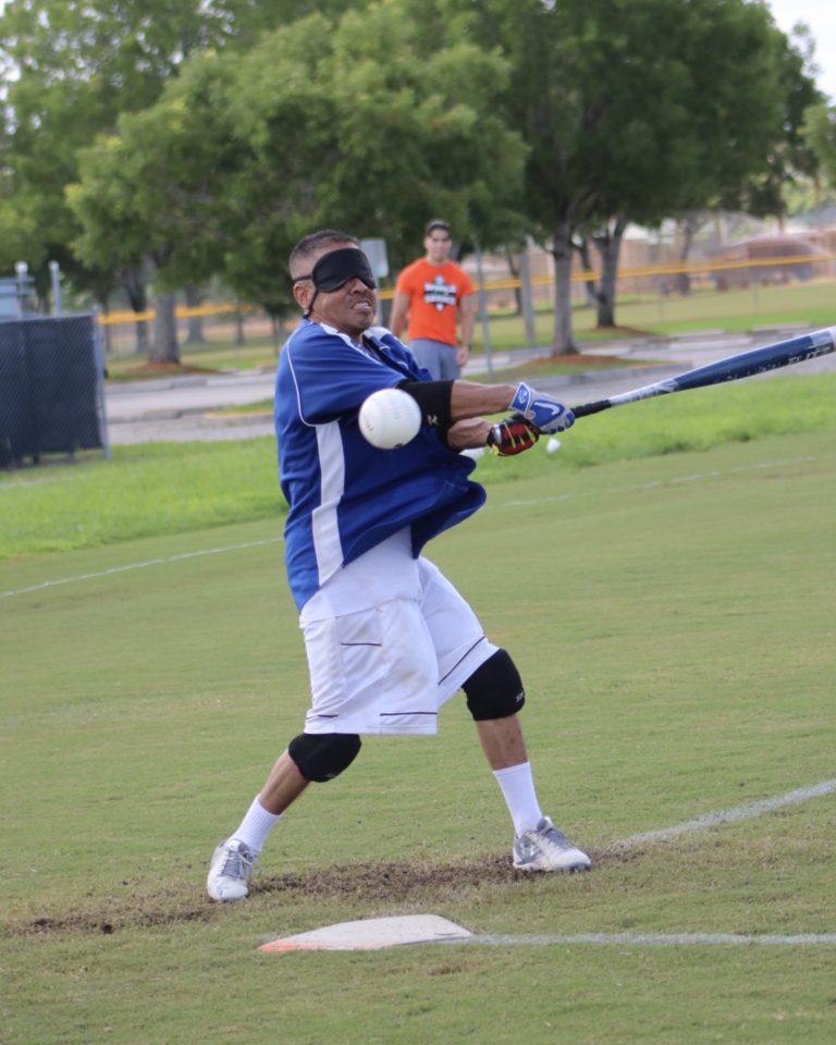 A player dressed in blue swings the bat as a ball hurdles towards him.