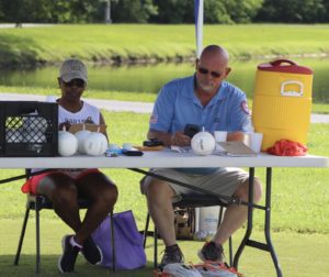 Umpire Mike Woodard takes a break from the sun to check messages while his volunteer finishes tallying scores.