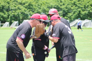 Austin Blackhawks Coaches and Pitcher and Catcher discussing "strategy" with their gloves over their mouths.