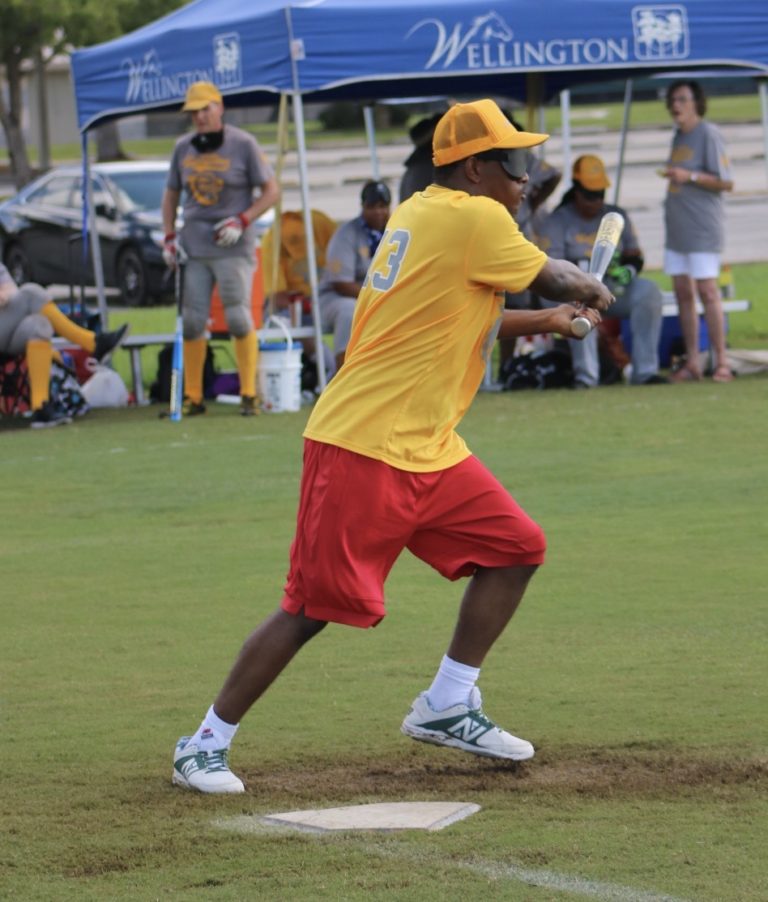 A player dressed in yellow swings the bat to the side as he launches off of home plate.