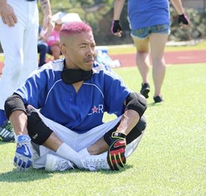 Ozzy Calamaco with the Lonestar Road Runners with pink hair sits cross-legged on the sidelines while watching a game.