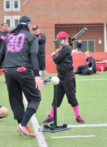 Tatyana Contreras, age 11, in batting stance with Brandon Chesser opposite the tee coaching her as she swings.