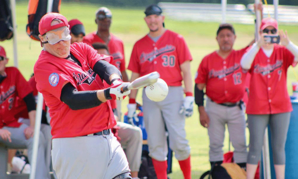 Austin Blackhawks batter makes contact with the ball as teammates watch from the bench behind.